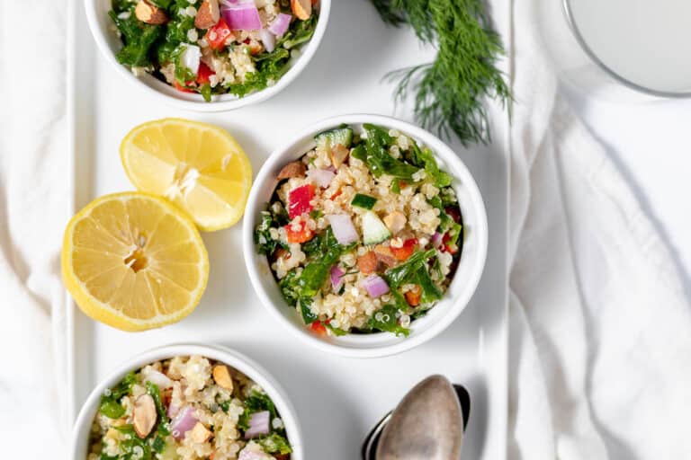 Top view of three bowls with quinoa salad garnished with lemon wedges on a white surface.