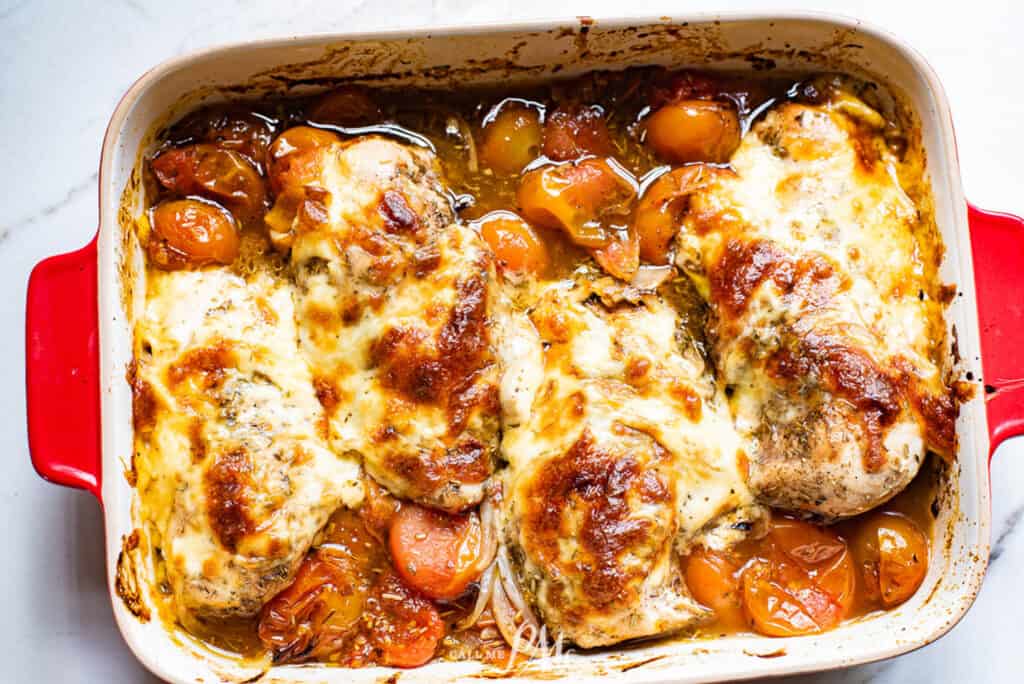 A red baking dish with chicken and tomatoes in it.