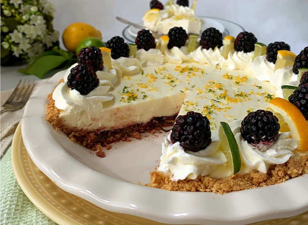A citrus cheesecake garnished with whipped cream and blackberries, with zest sprinkled on top.