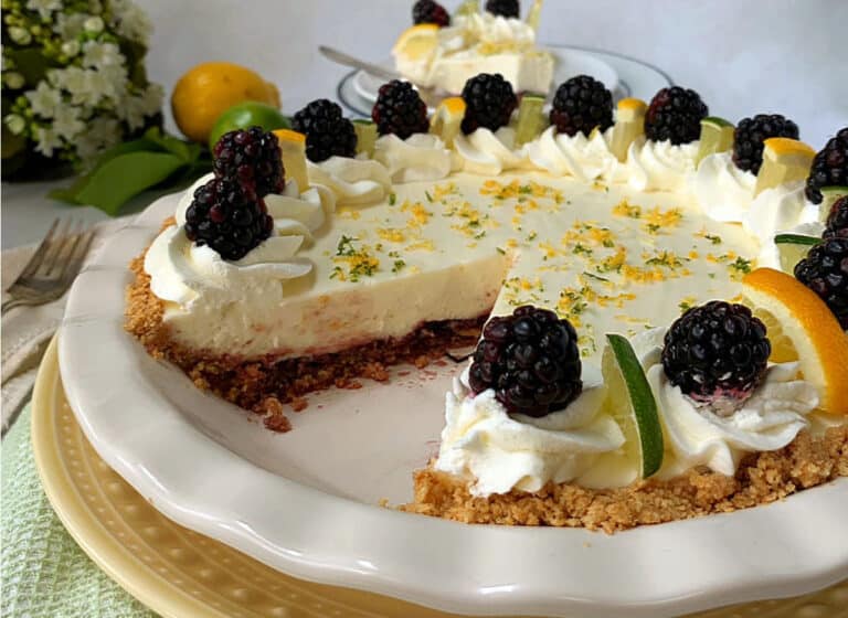 A citrus cheesecake garnished with whipped cream and blackberries, with zest sprinkled on top.