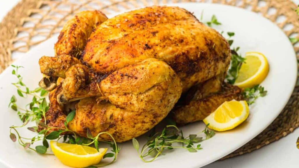 Roasted chicken served on a white plate with lemon slices and herbs.