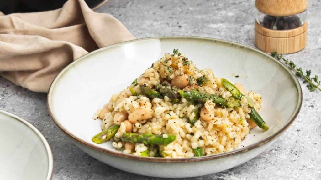 Plate of risotto with asparagus and beans garnished with herbs on a minimalist table setting.