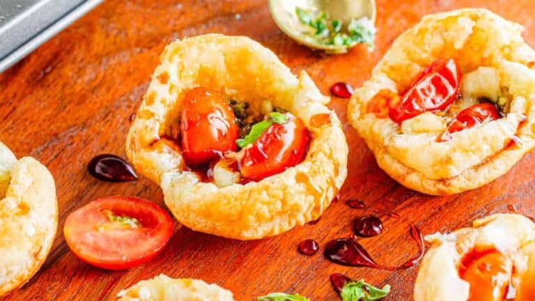 Fresh cherry tomatoes and herbs served in crispy puff pastry cups on a wooden surface.