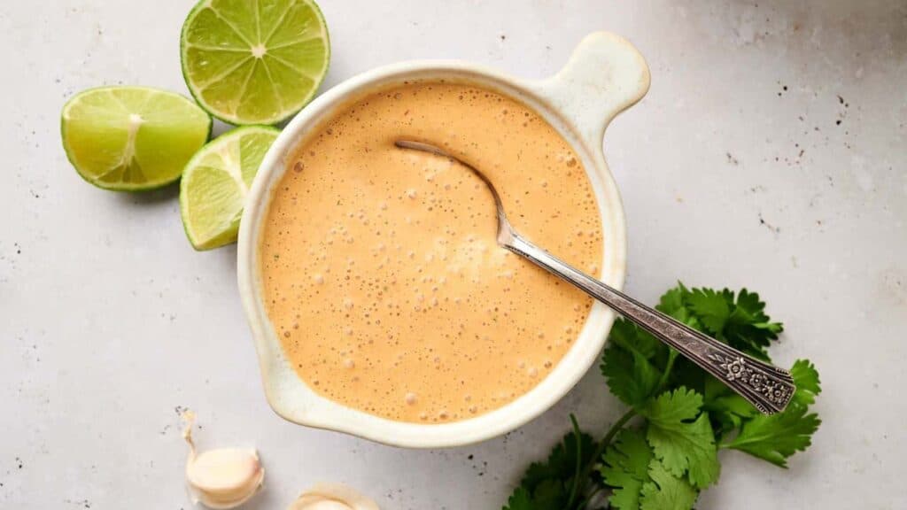 A bowl of creamy salad dressing with garlic, lime, and cilantro on a light surface.