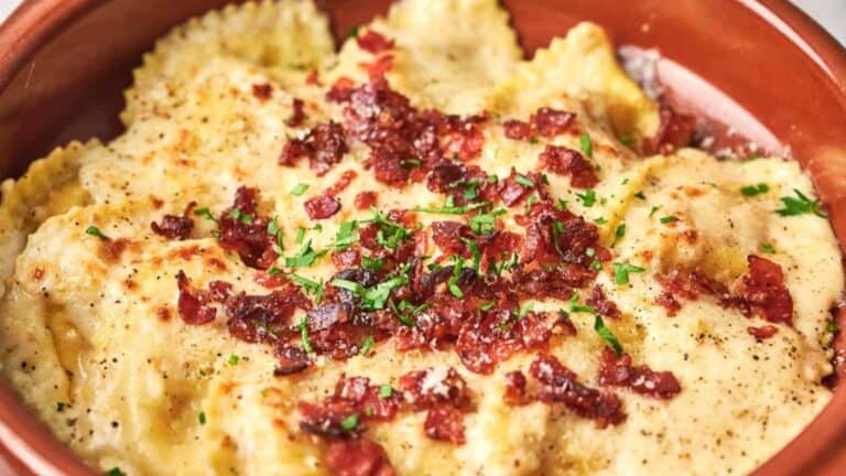 Plate of ravioli topped with cheese, bacon bits, and chopped herbs.