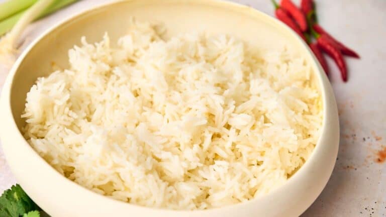 A bowl of cooked white rice on a table, with chili peppers in the background.