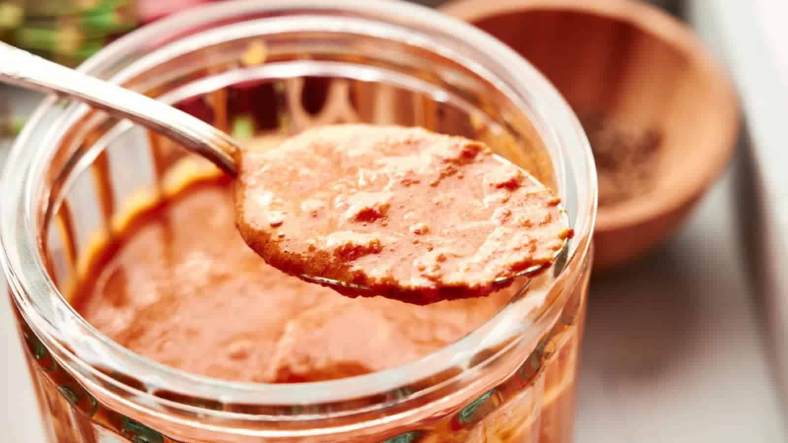 A spoon lifting a serving of chunky Thai red curry paste from a jar.