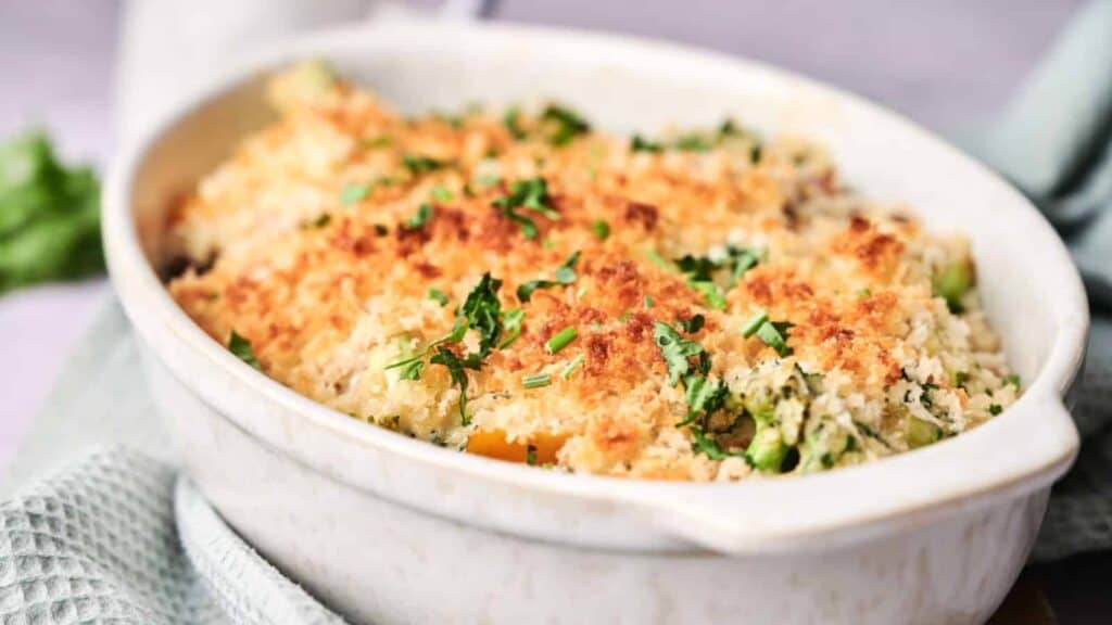 Baked casserole with a golden-brown crumb topping and garnished with chopped herbs.