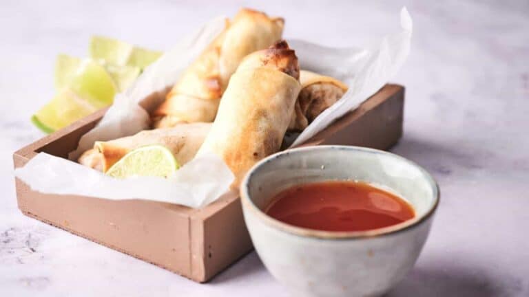 Golden spring rolls served with lime wedges and dipping sauce.