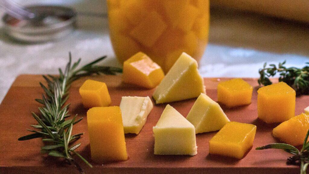 Sliced cheese and mango cubes arranged on a wooden cutting board with sprigs of rosemary.