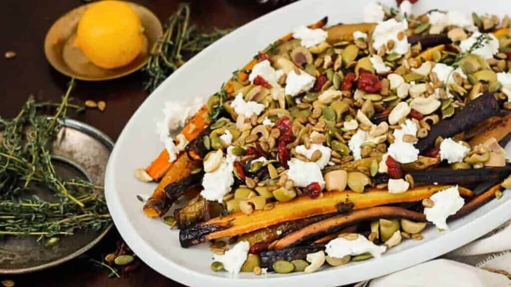 Oven-roasted carrots topped with crumbled cheese and mixed nuts, served on a white platter.