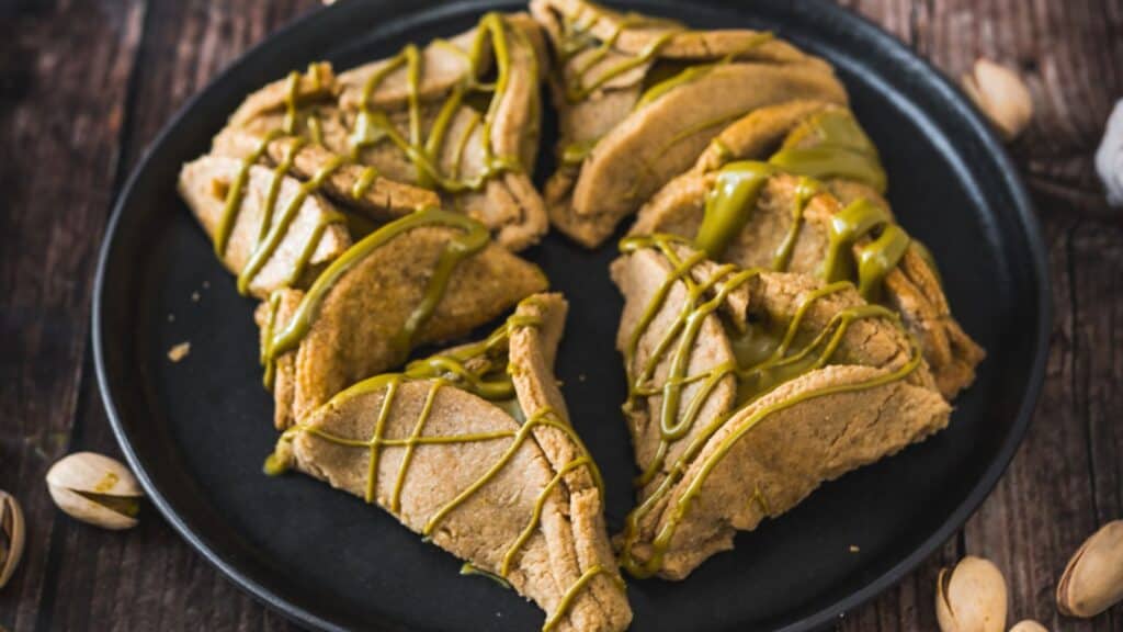 Slices of pistachio-flavored cookies drizzled with green tea glaze, presented on a round black plate.