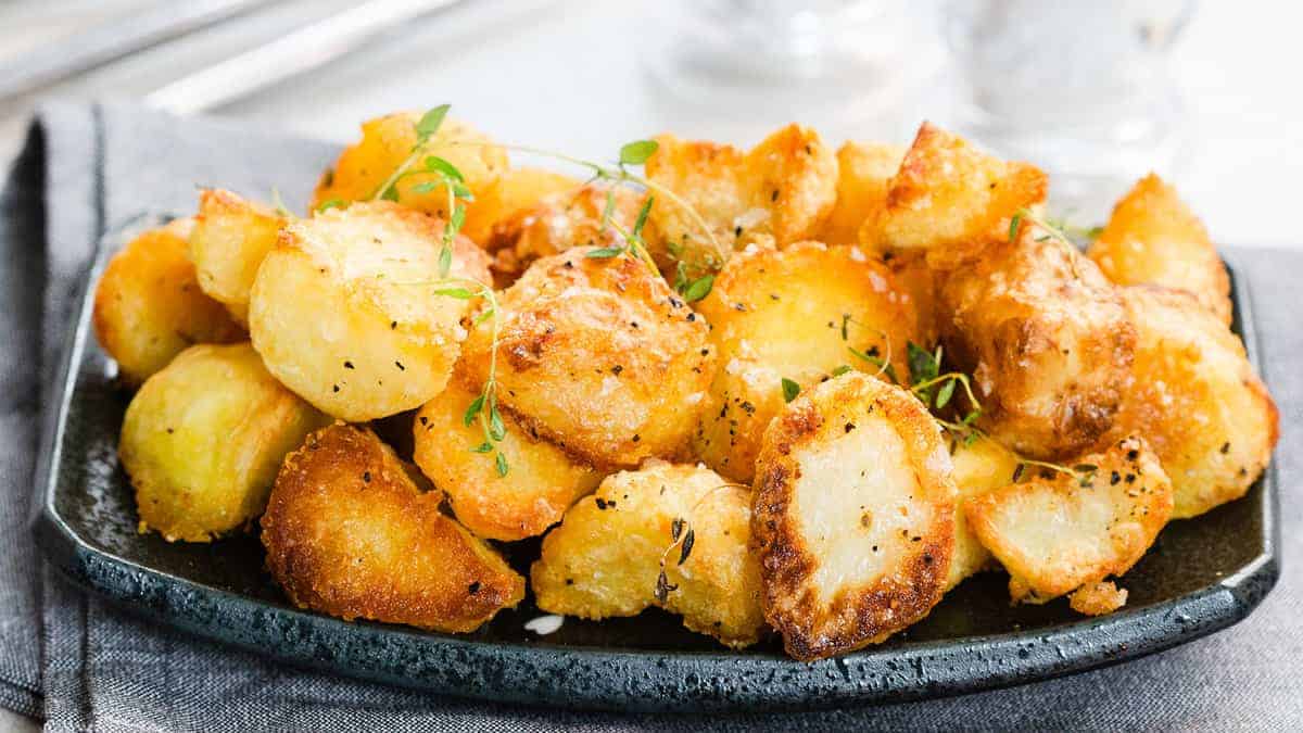 A close up image of a plate piled high with crispy roasted potatoes garnished with fresh thyme.