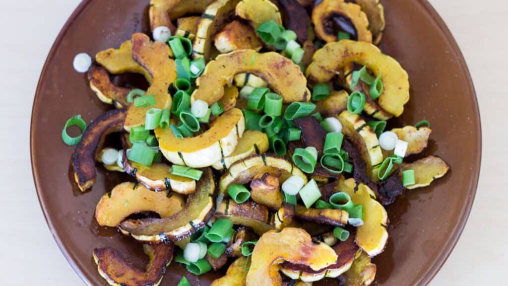 Roasted squash with scallions on a brown plate.