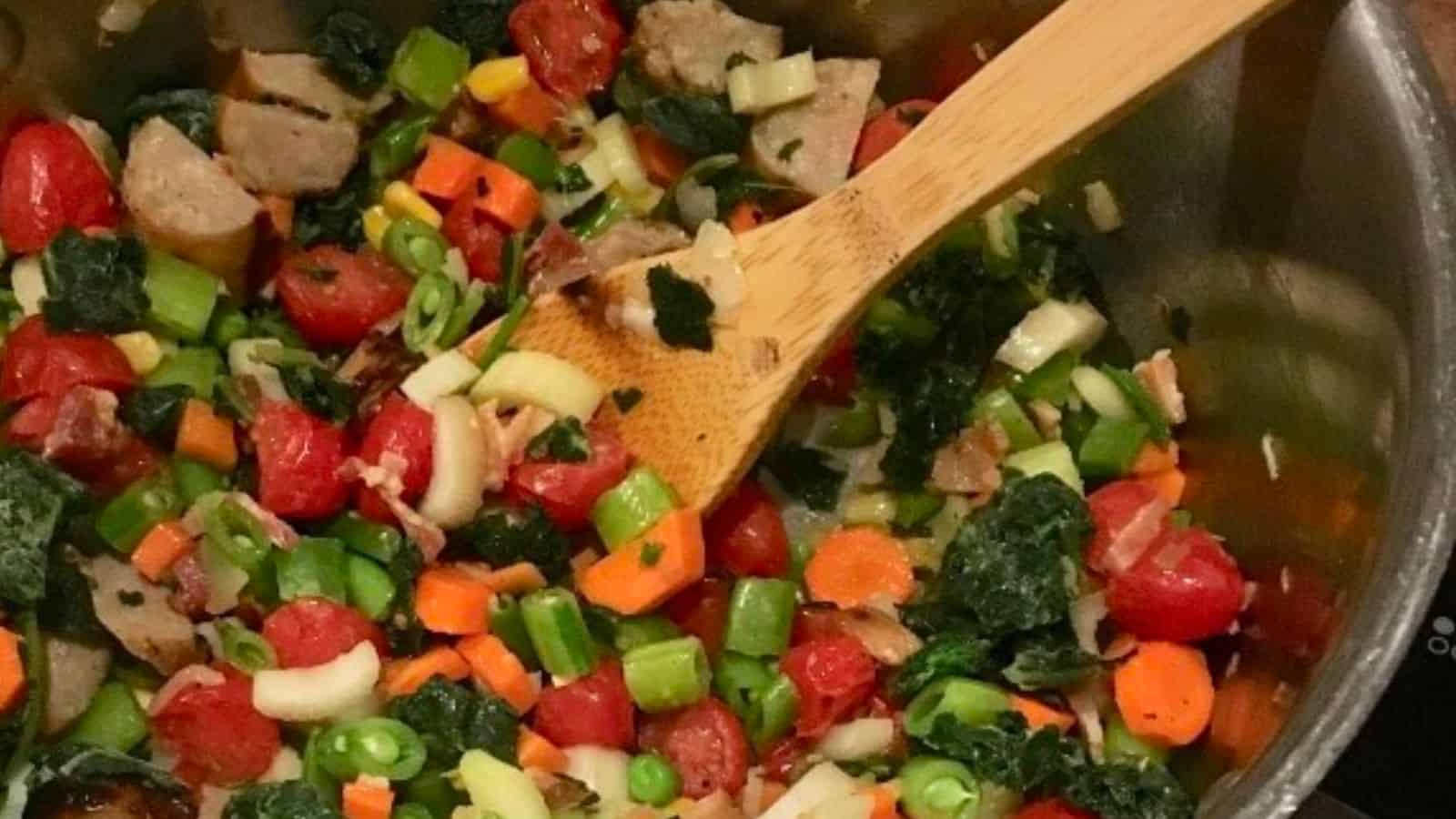 Sausage, kale and bean soup in pot with a wooden spoon.