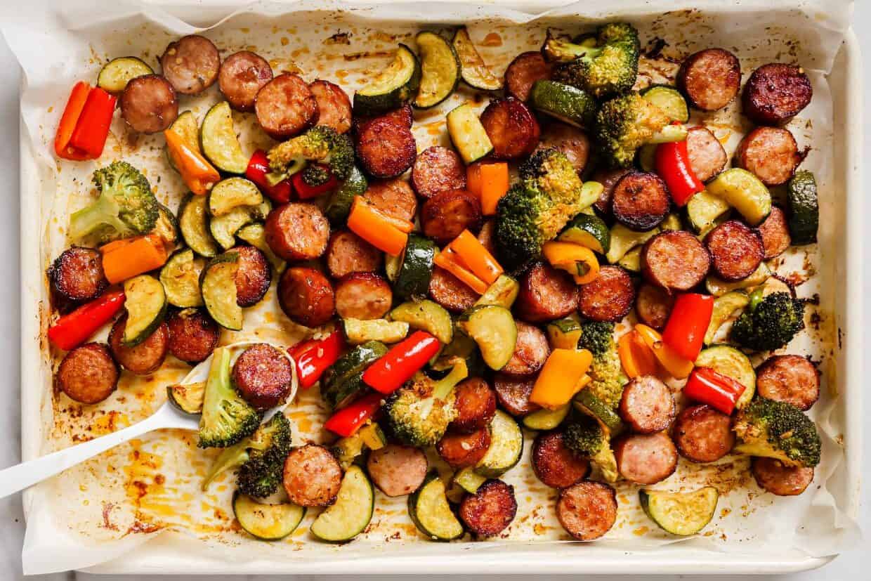 Sausage and veggies sheet pan dinner with a spoon.