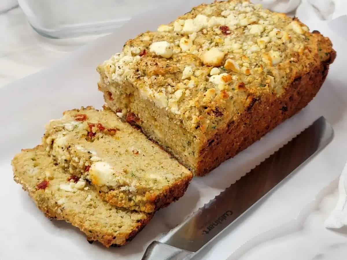 A loaf of savory quick bread sliced on a piece of parchment paper.