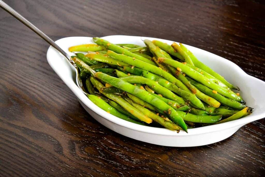 Sautéed green beans in a white serving dish with a fork.