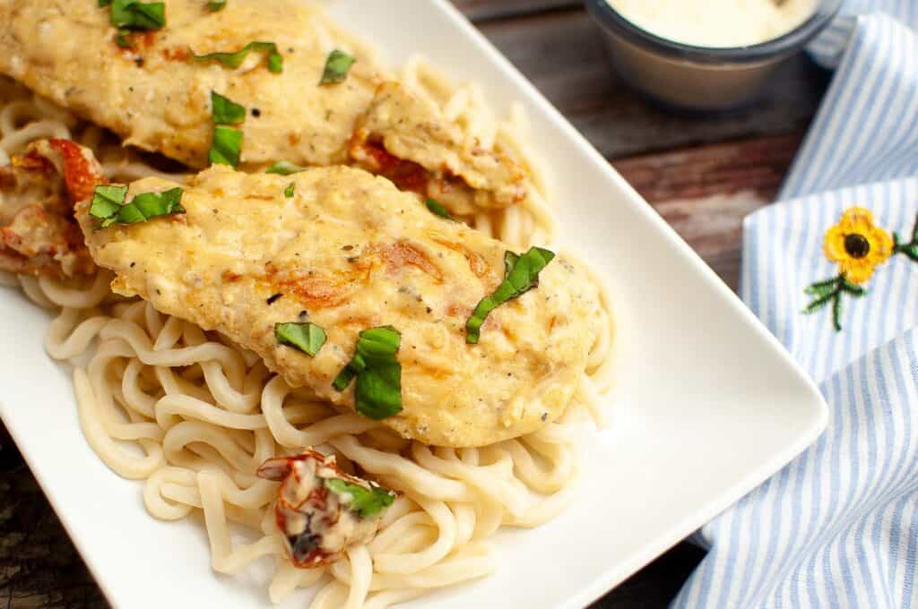 Grilled chicken breasts served over pasta garnished with fresh herbs.