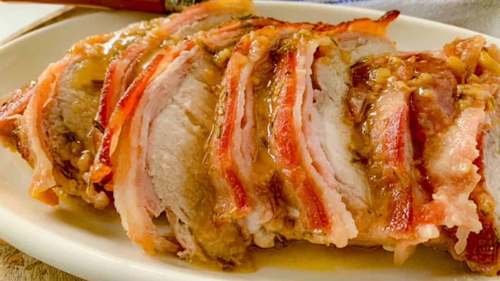 A platter piled with bacon-wrapped pork tenderloin slices and pan juices.