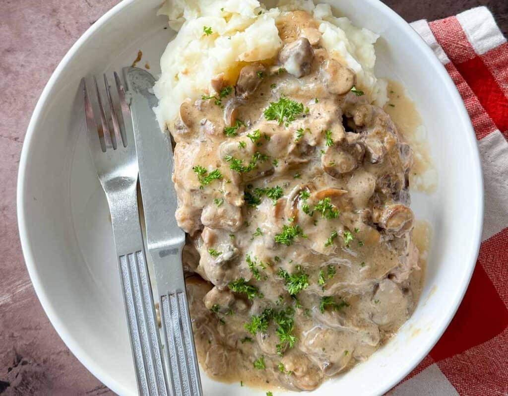 A plate of creamy beef stroganoff served over mashed potatoes, garnished with parsley.