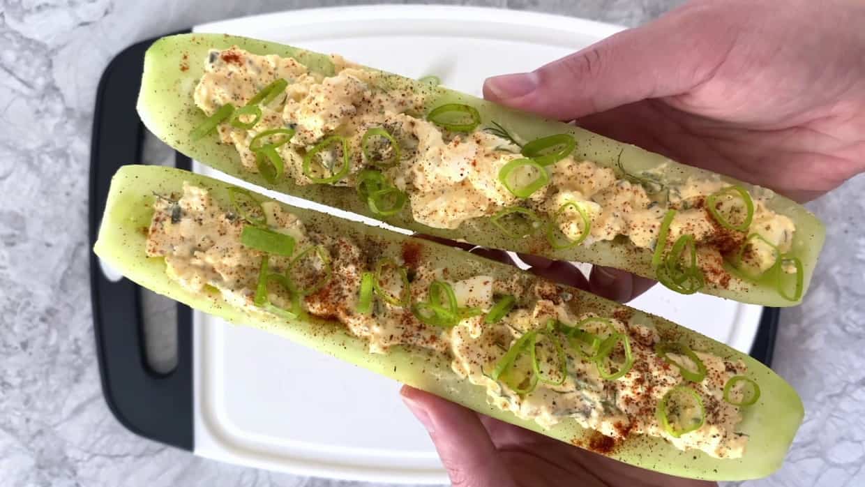 Spicy egg salad cucumber boats being held in hands.