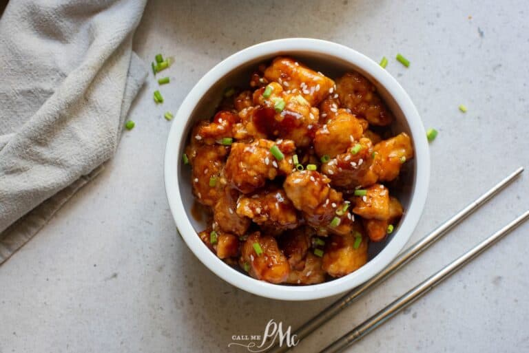 A bowl of asian chicken in a white bowl with chopsticks.