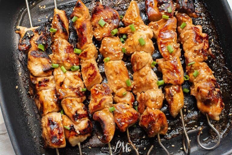 Asian chicken skewers on skewers in a pan.