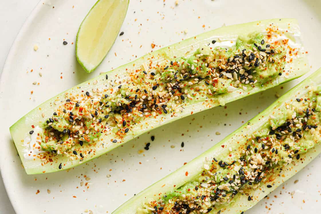 Tajin cucumber boats on a plate next to a slice of lime.