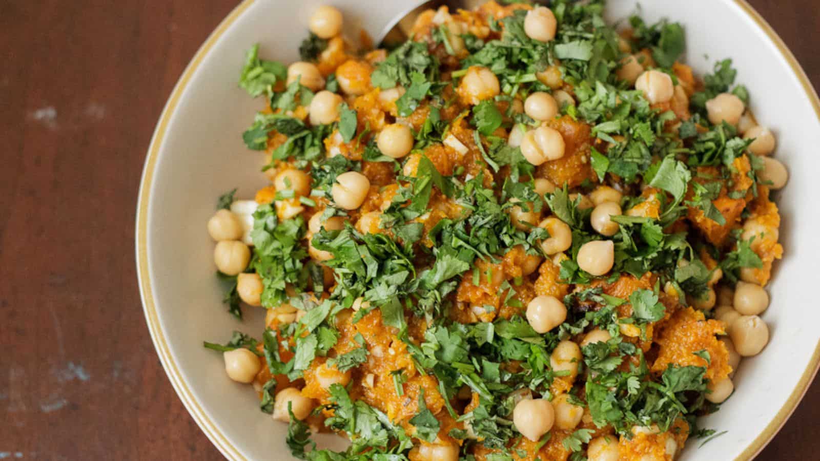 A bowl of chickpea salad garnished with chopped cilantro on a wooden surface.