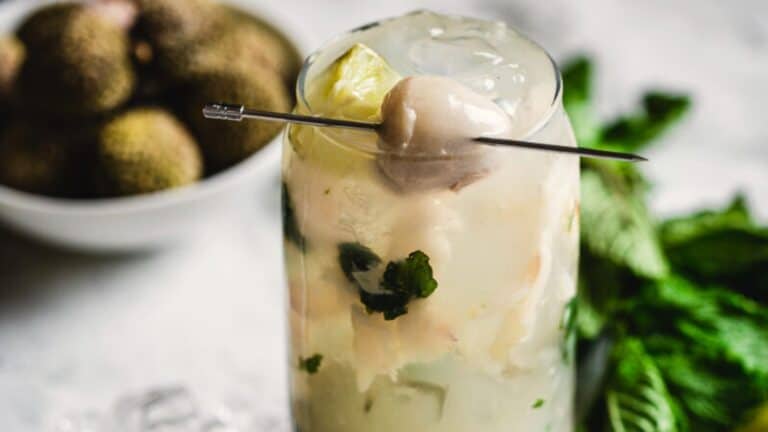 A refreshing cocktail garnished with a lychee and mint leaves, served on a table.