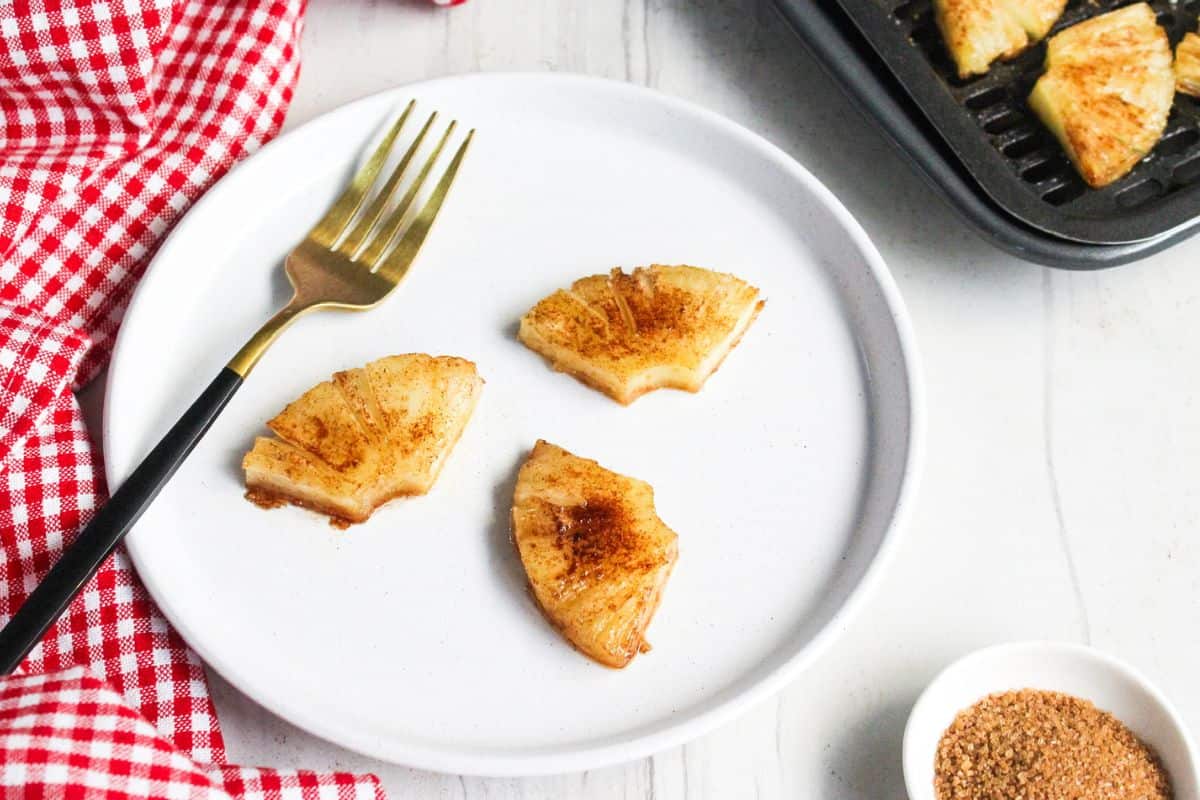 Three pieces of air-fried pineapple on a white plate with a fork.