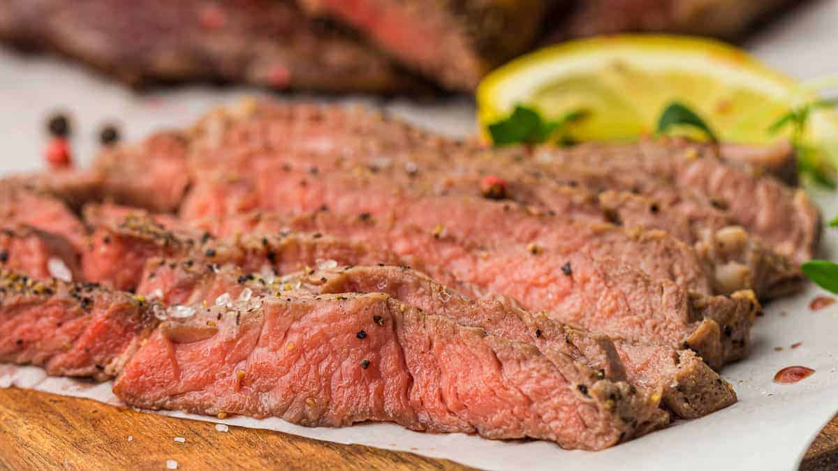 Sliced steak on a cutting board with lemon wedges.