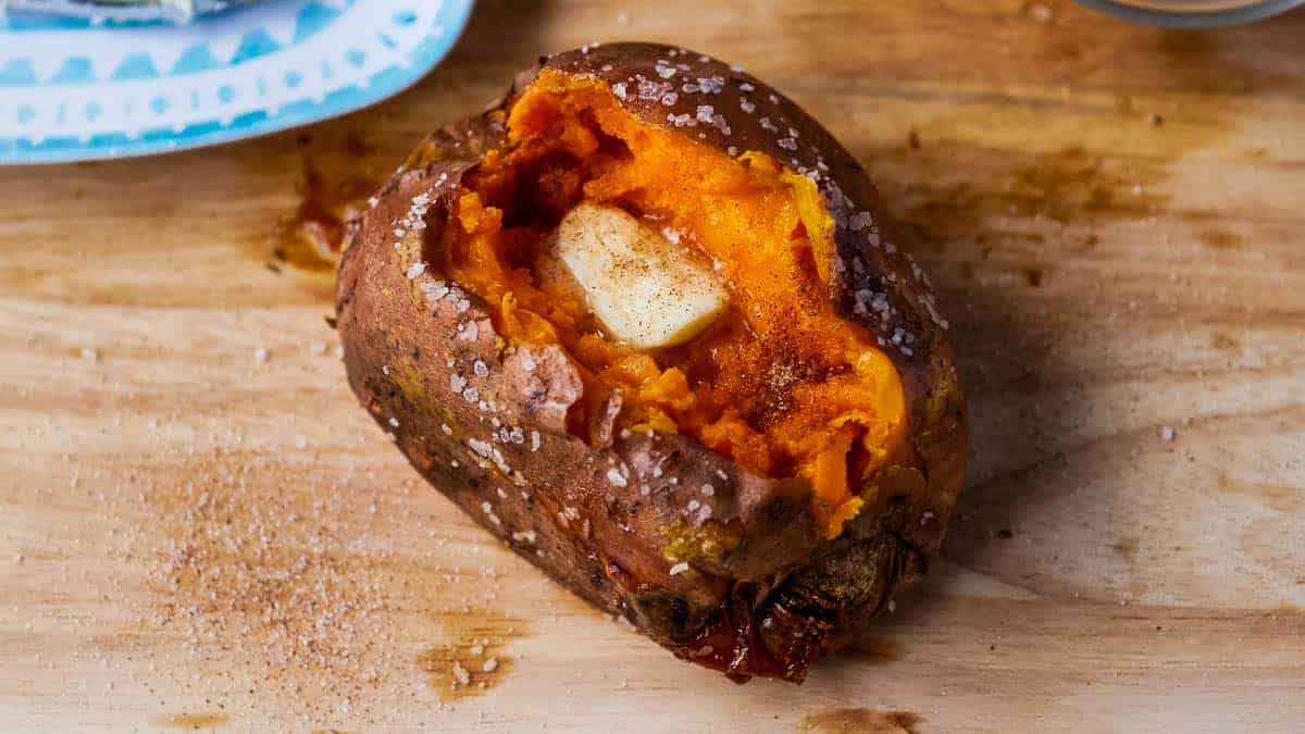 Baked sweet potato with butter with a bowl of cinnamon sugar and a plate of butter in the background.