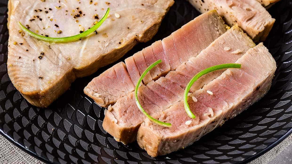 Slices of seared tuna garnished with green onion on a black plate.