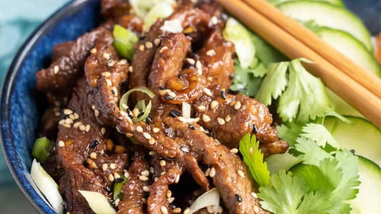 A bowl of sesame-covered beef stir-fry with cucumbers and coriander, served with chopsticks.