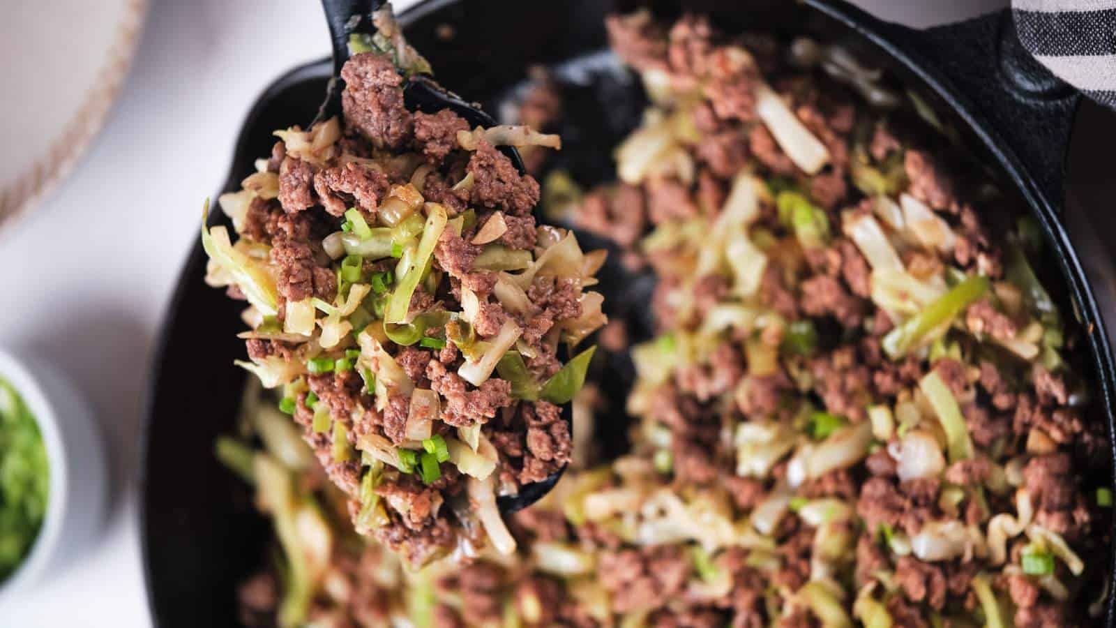 Ground beef and cabbage stir fry being scooped out from a skillet.