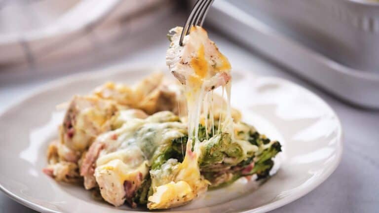 Fork lifting a cheesy bite from a plate of baked chicken and broccoli casserole.