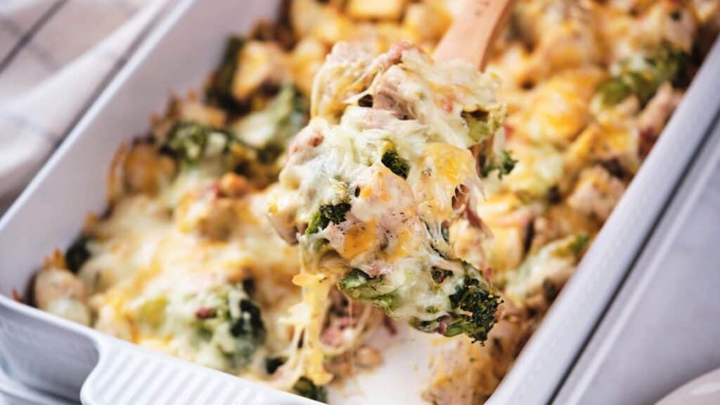 A scoop of cheesy broccoli casserole being taken from a baking dish.