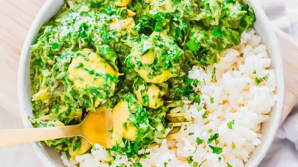 A bowl of white rice topped with creamy spinach and chicken.