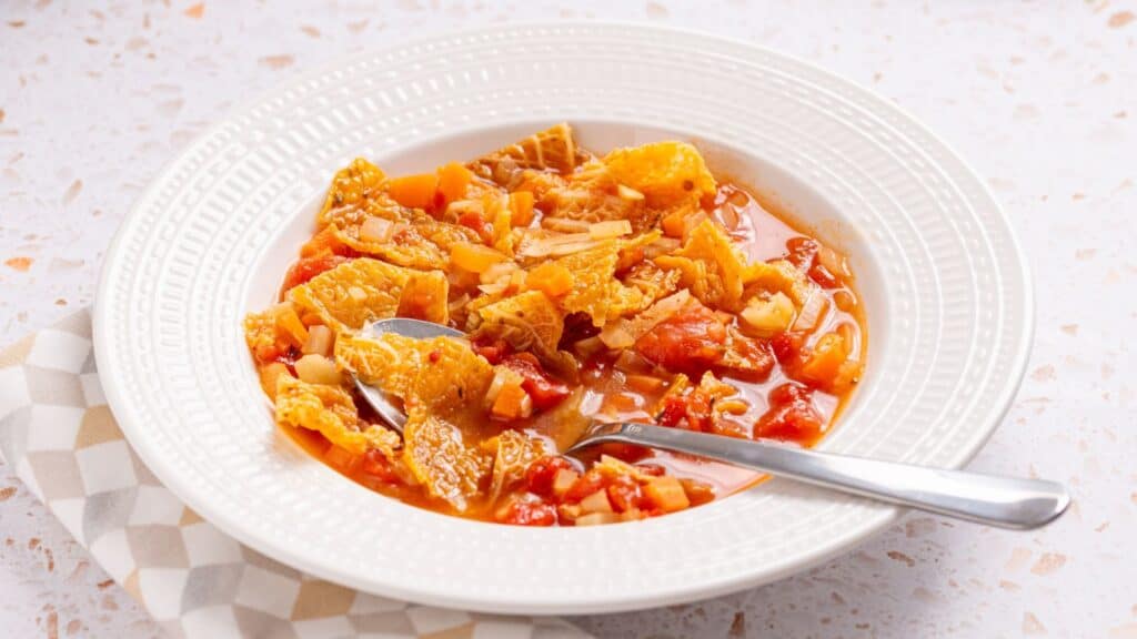 A bowl of hearty tomato-based vegetable stew with a spoon.