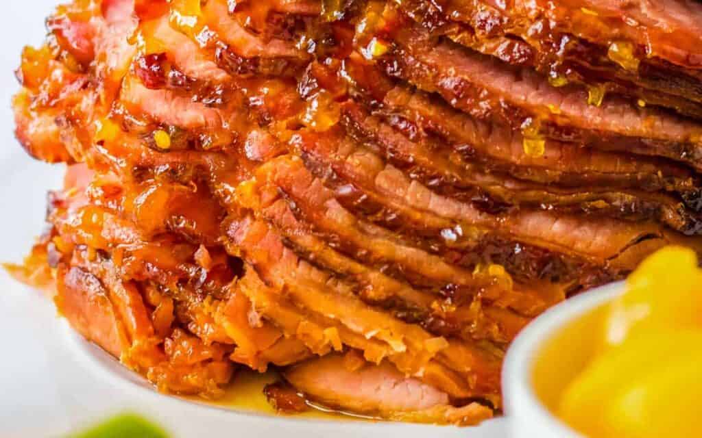 Close-up of a glazed, spiral-cut ham with a piece of lemon on the side.