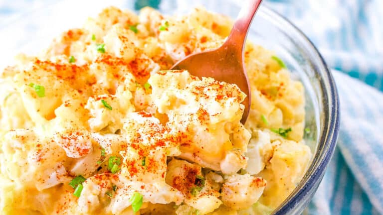 A bowl of creamy potato salad garnished with paprika and chopped green onions.