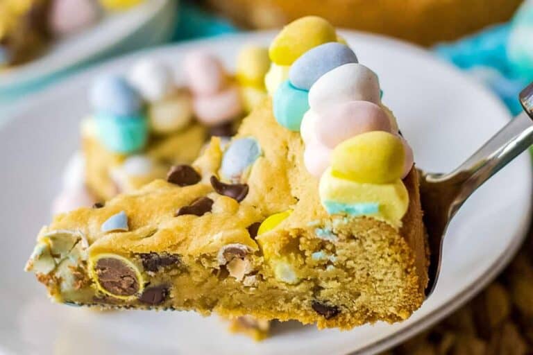 A slice of cookie cake decorated with colorful candy and chocolate chips on a plate with a fork.