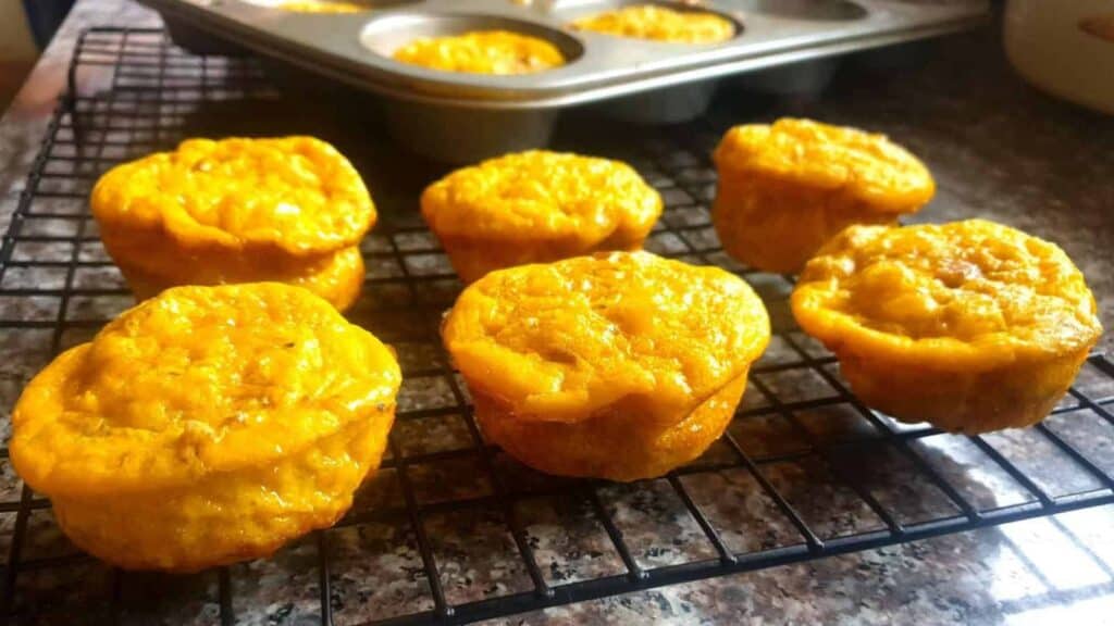 Homemade muffins cooling on a wire rack with a muffin tin in the background.