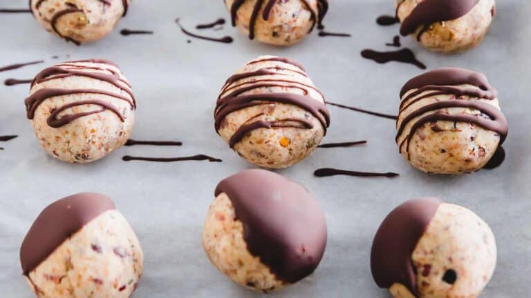 Chocolate drizzled cookies half-dipped in dark chocolate on parchment paper.