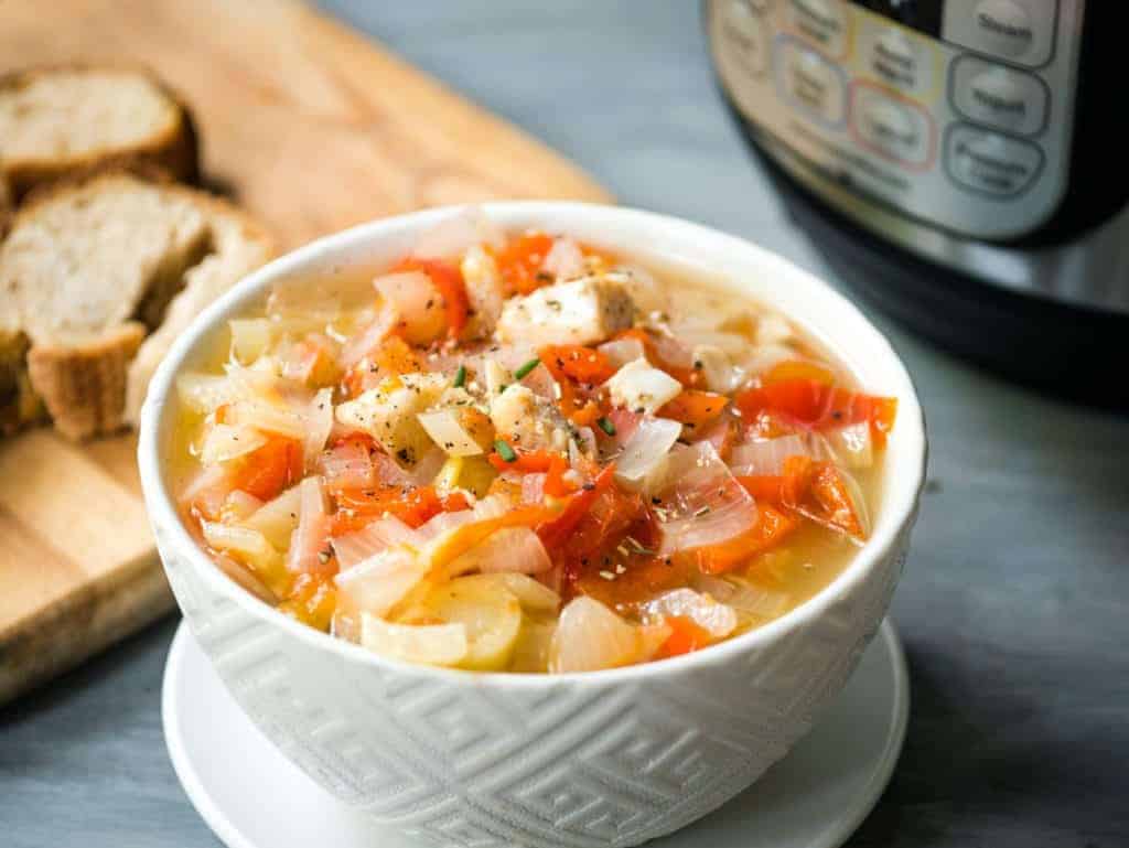 Fish stew with tomatoes and onions in a white bowl.