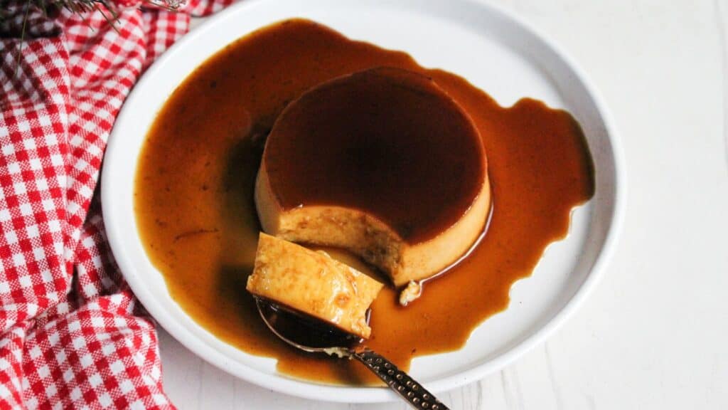A caramel flan on a white plate with caramel sauce spilled over the sides.