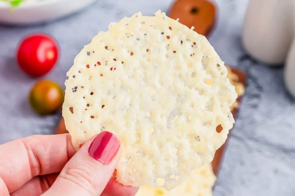 Hand holding a crispy cheese cracker with visible herbs and spices.
