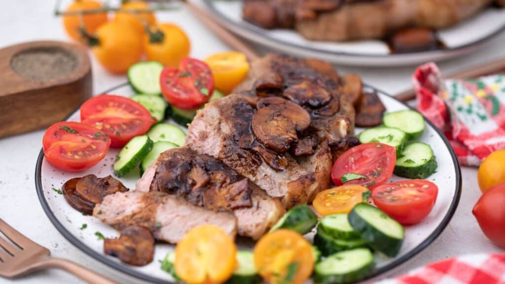 Grilled pork chops with mushrooms served alongside a fresh tomato and cucumber salad.